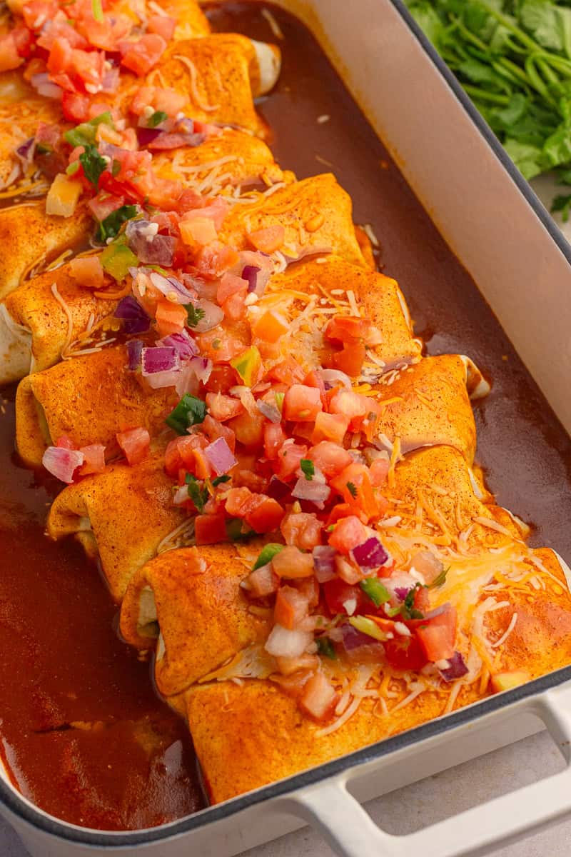 Baked enchiladas in a dish, topped with pico de gallo and fresh cilantro.