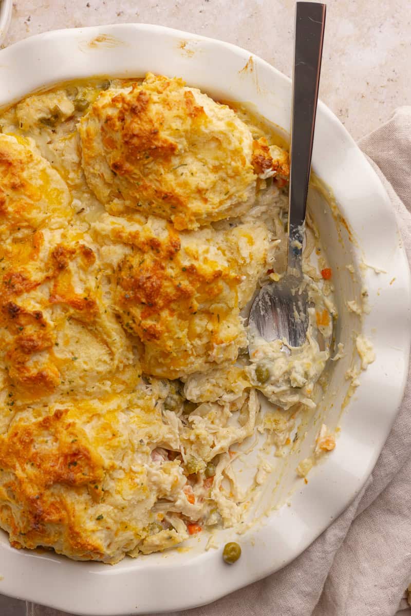 A spoon scooping into the creamy chicken pot pie with flaky, cheesy biscuits on top.