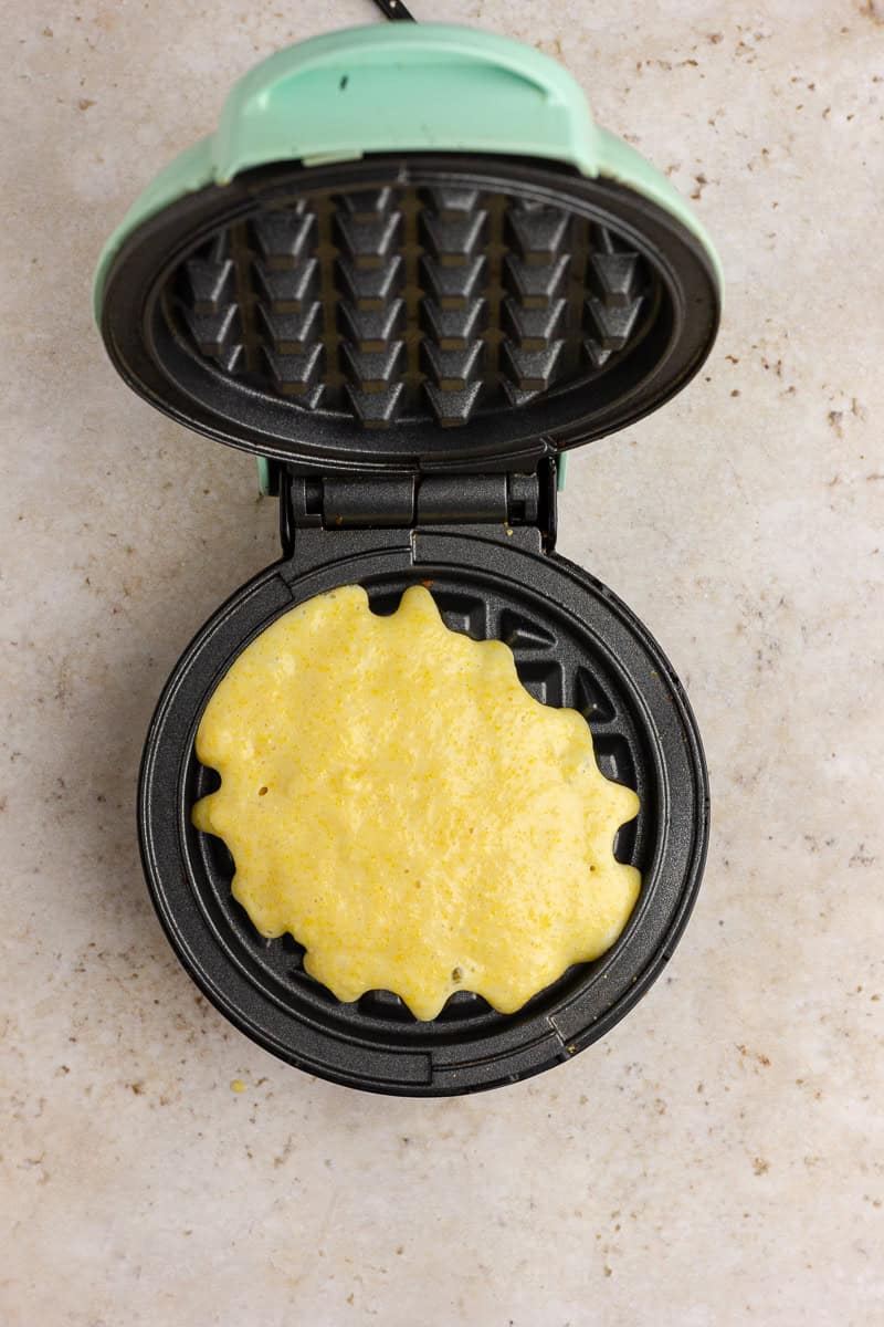 Cornbread waffle batter poured into a mini waffle maker, ready to cook.