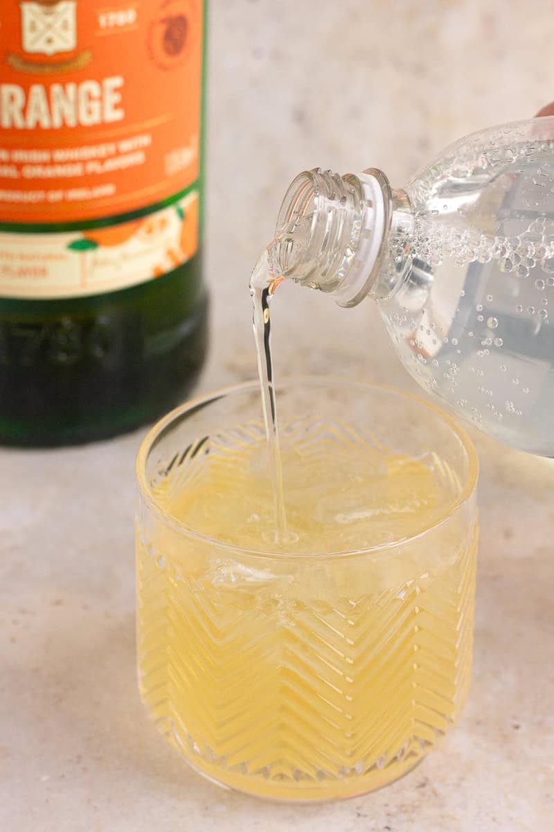 Club soda being poured into a glass filled with Jameson Orange and lemonade.