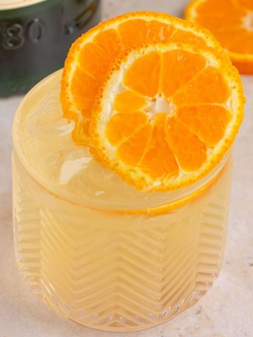 A close-up of the final cocktail with vibrant orange slices on top, with a Jameson Orange bottle in the background.
