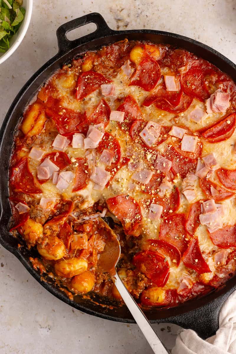 A serving spoon scooping out a cheesy, saucy bite of Pizza Gnocchi from the skillet.