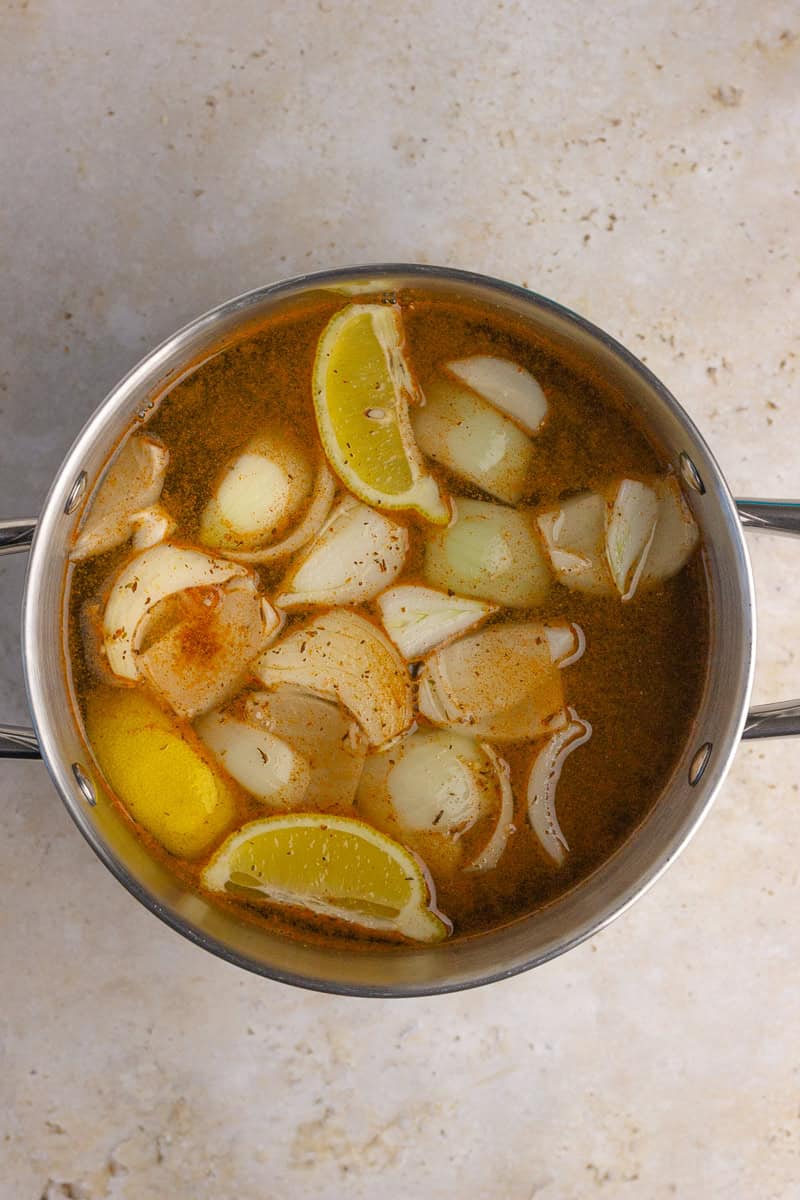 A pot filled with seasoned broth, lemon wedges, and onion slices for a shrimp boil.