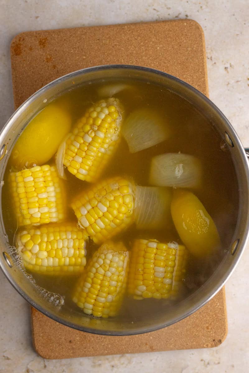 Corn on the cob and onion pieces boiling in a large pot of seasoned water.