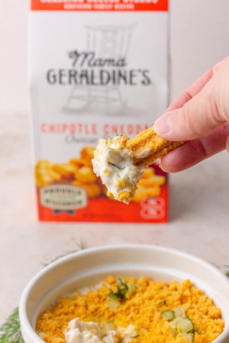 A hand dipping a cheese straw into Southern Fried Pickle Dip, showing creamy texture.