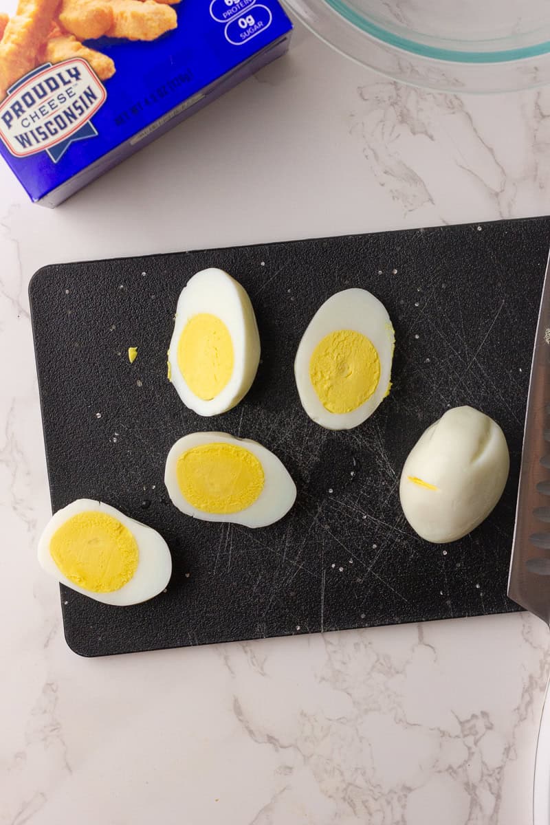 Hard-boiled eggs sliced in half on a cutting board, ready to be made into deviled eggs.