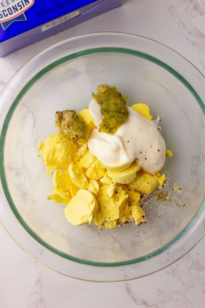 Deviled egg filling ingredients including yolks, mayo, mustard, and relish in a glass bowl.