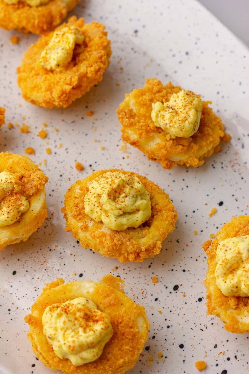 Close-up of air fried deviled eggs on a speckled platter with golden coating and yolk filling.