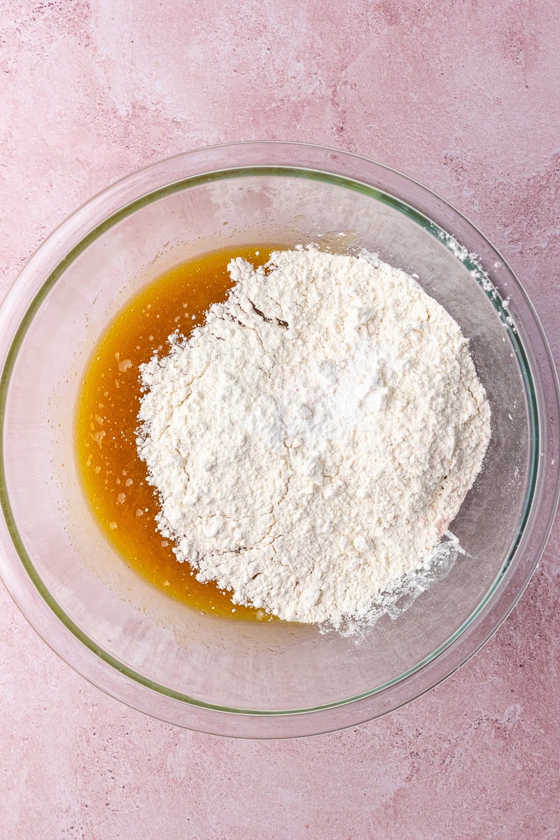 The dry ingredients, including flour, baking powder, and salt, are added to the wet mixture in the bowl.