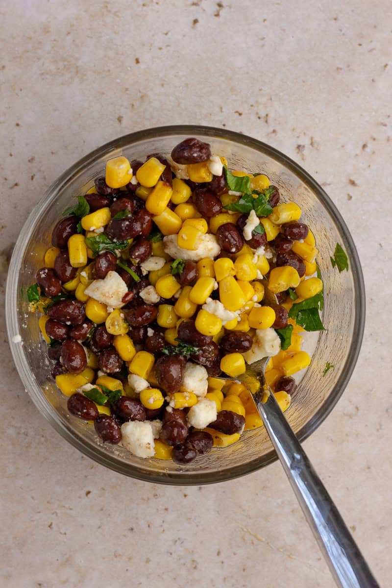 Black bean corn feta dip fully mixed in a glass bowl with a spoon.