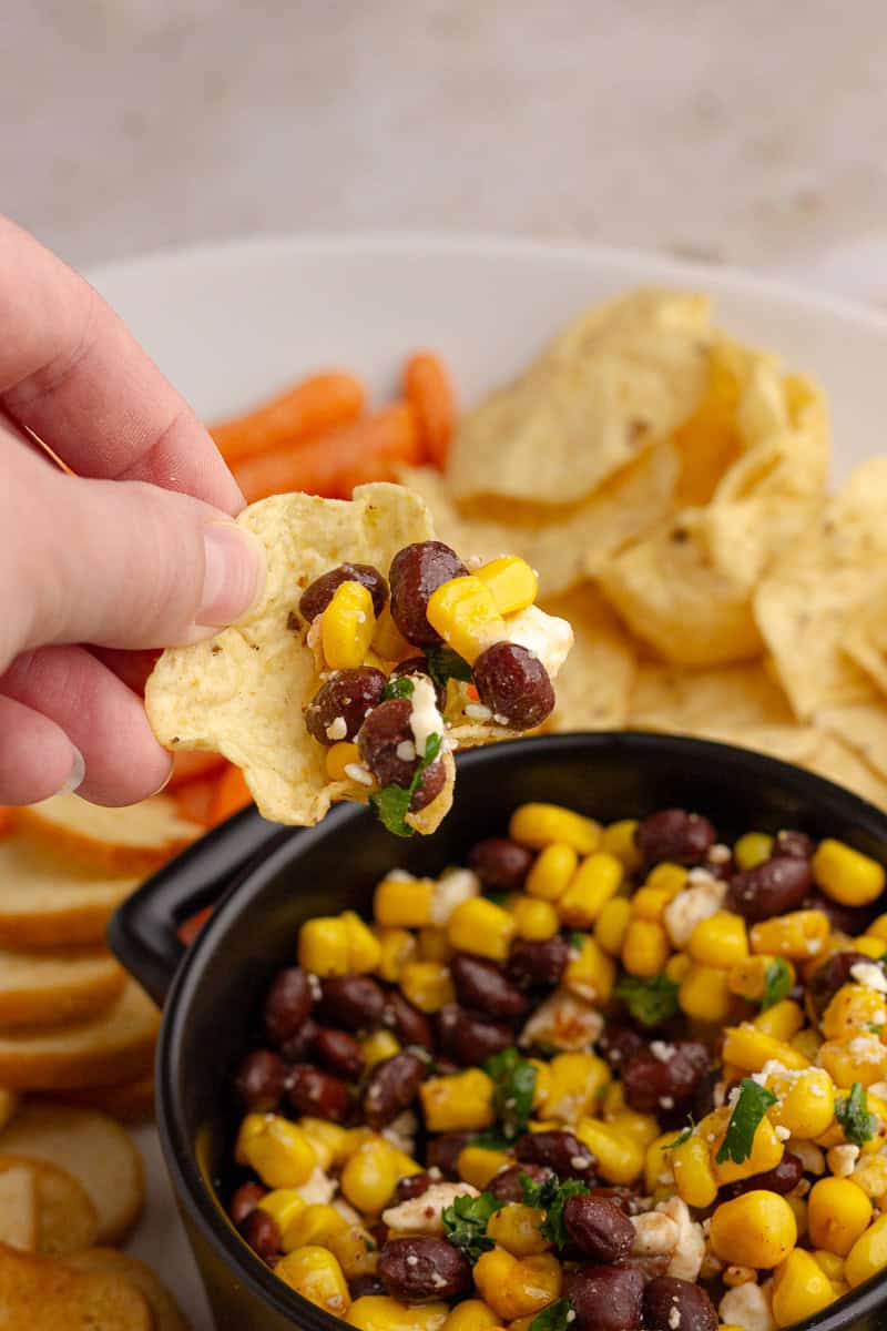 Hand with tortilla chip scooping up the dip from a serving bowl.