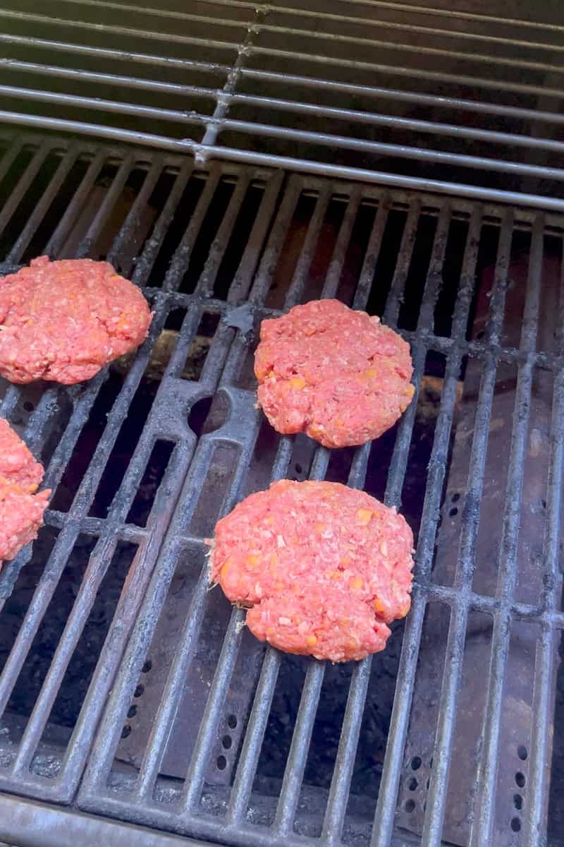 Uncooked chipotle cheese burger patties sizzling on a hot outdoor grill grate.