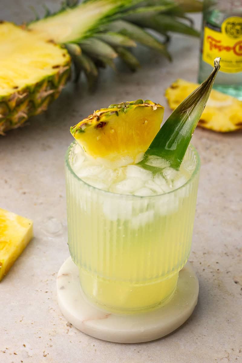 A refreshing pineapple ranch water cocktail served over ice with a pineapple wedge and leaf for garnish.