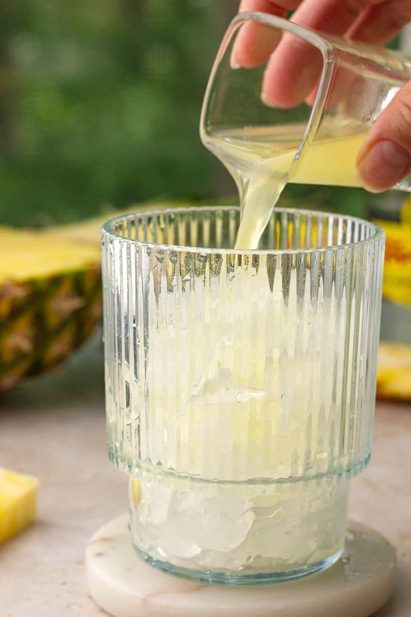 Pineapple juice being poured into a glass of ice to make pineapple ranch water.