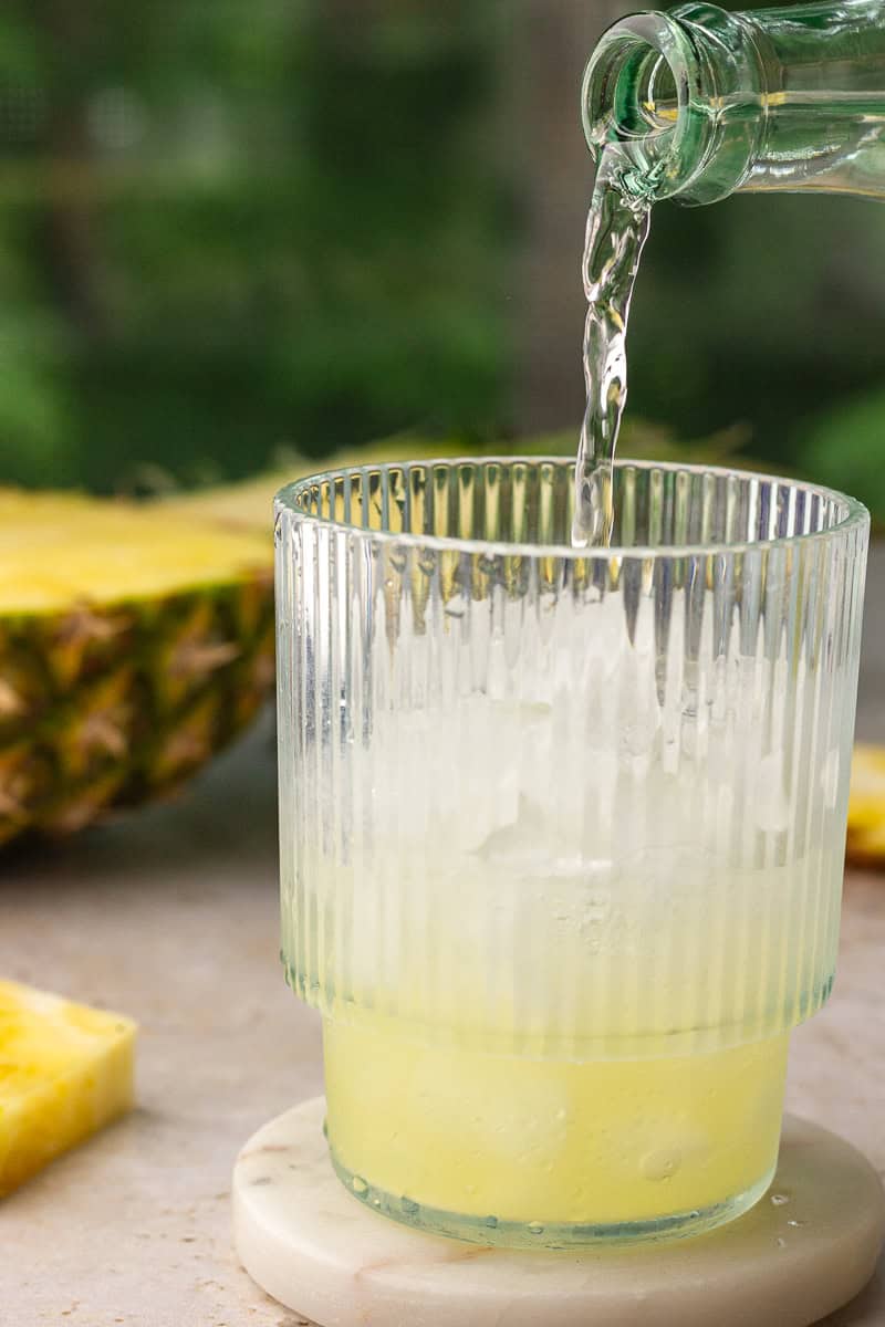 Sparkling Topo Chico being poured into a cocktail glass filled with pineapple and lime juice.