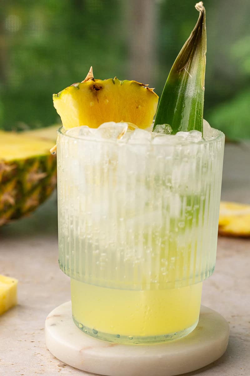 A close-up of the finished pineapple ranch water with bubbly fizz, pineapple wedge, and leaf.