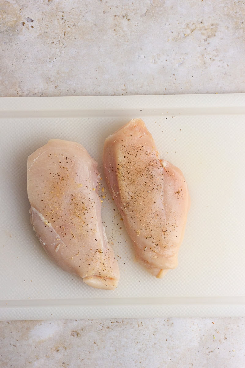 Seasoned raw chicken breasts on a cutting board, ready to be cooked.