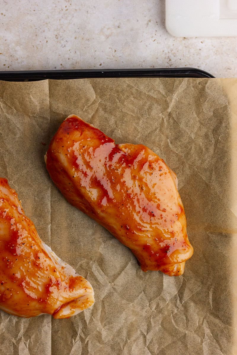 BBQ-coated chicken breasts placed on a parchment-lined tray before air frying.