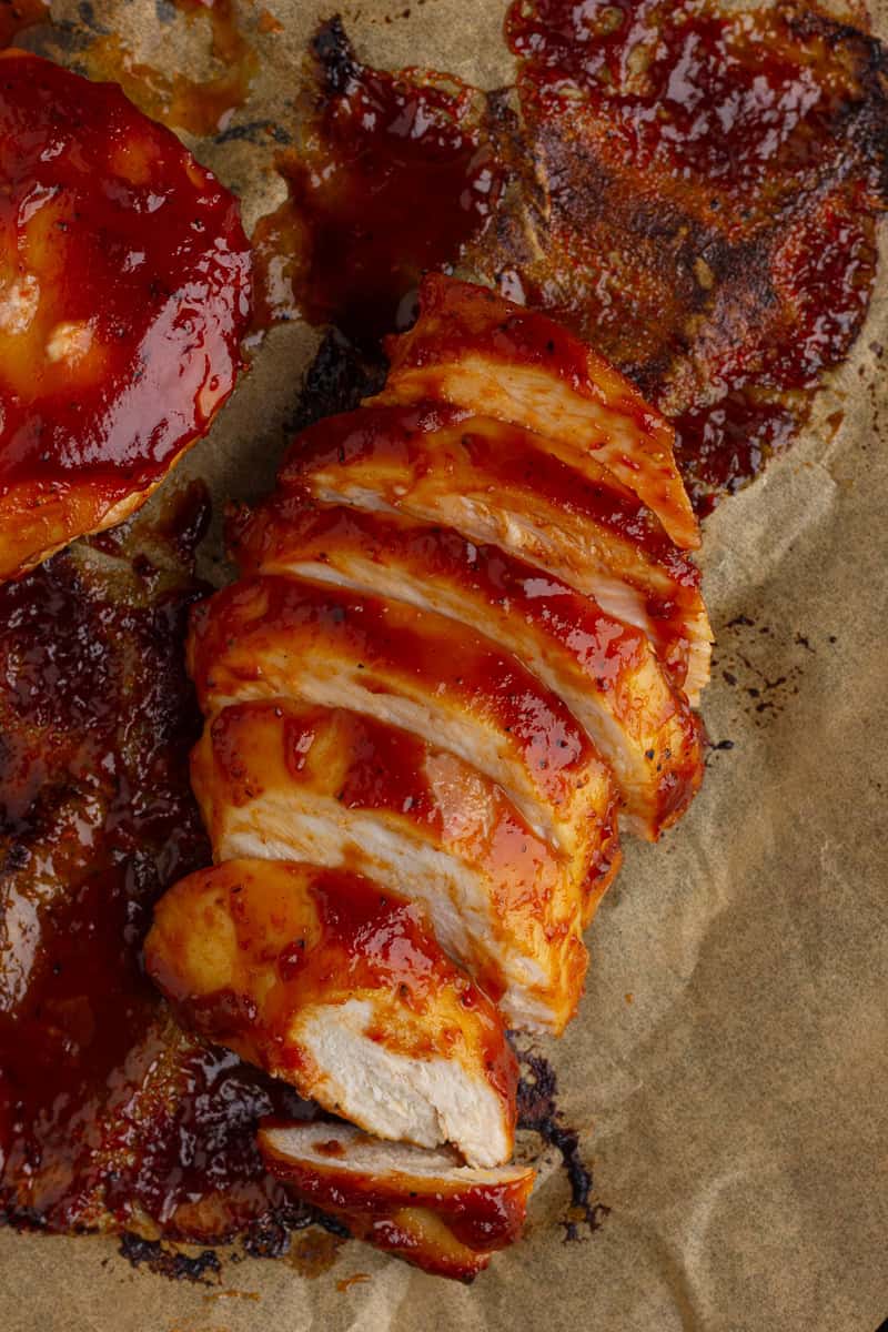 Perfectly cooked BBQ chicken breast sliced on a sheet of parchment with caramelized sauce.