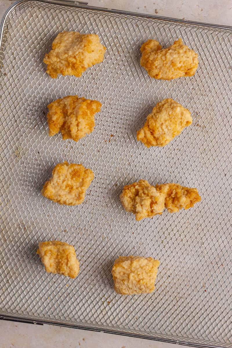 Cooked chicken nuggets arranged on an air fryer tray after crisping.