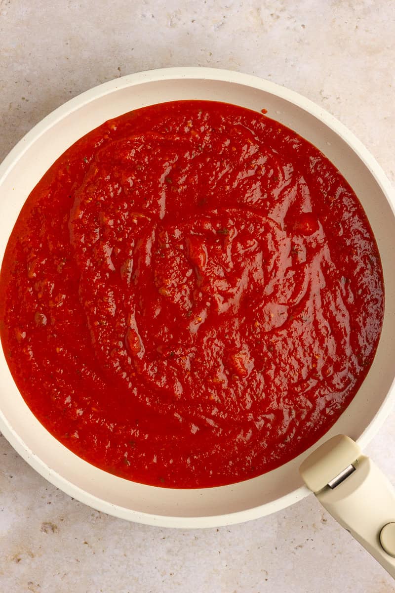 Marinara sauce heating in a white skillet, ready to be combined with other ingredients.