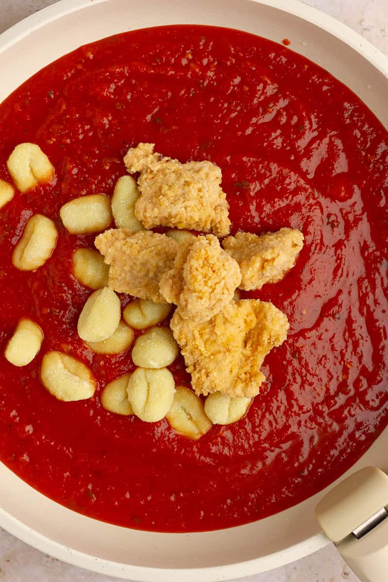 Gnocchi and chicken nuggets added to warm marinara sauce in a skillet.
