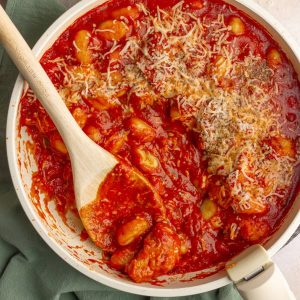Finished skillet of chicken parmesan with gnocchi, topped with melted cheese and herbs.