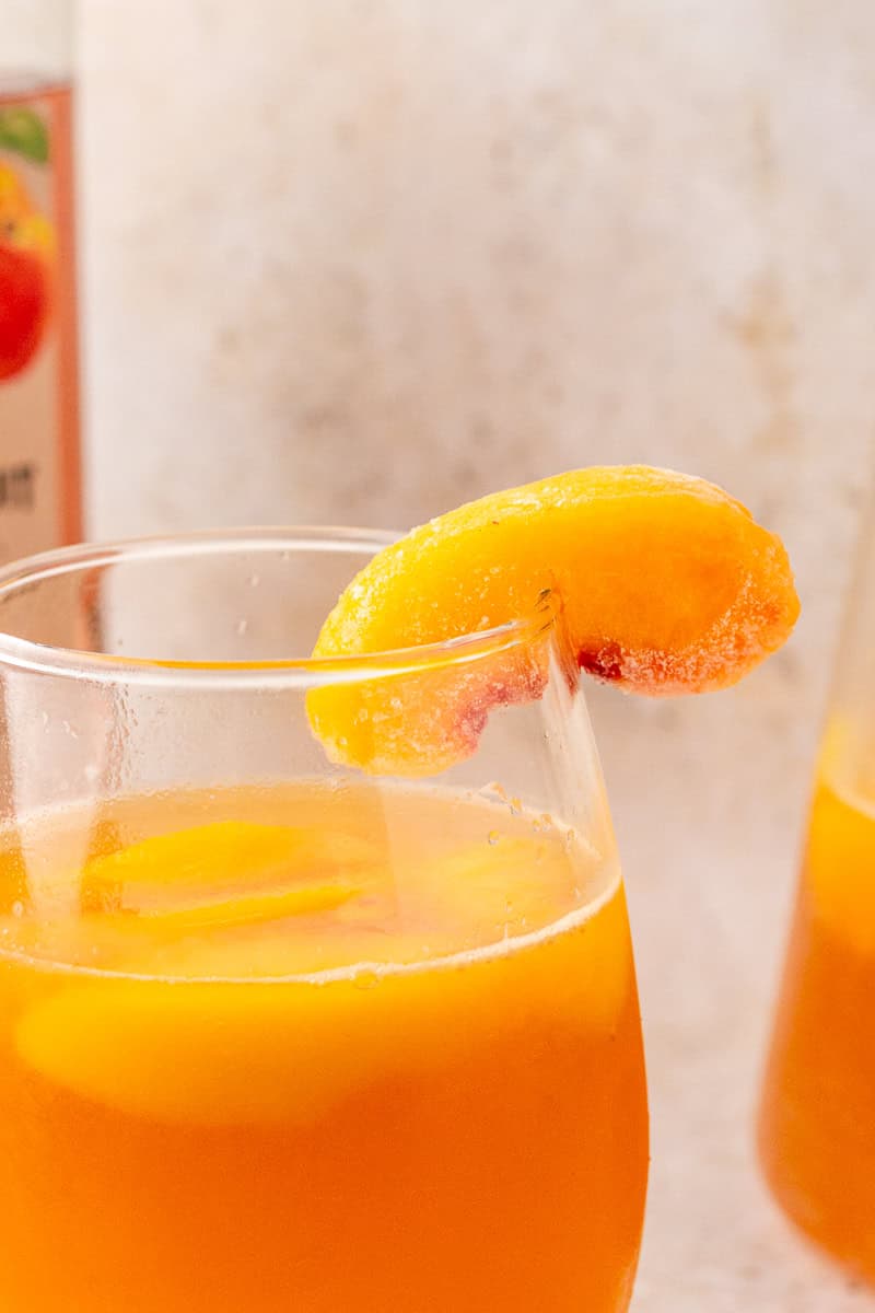Close-up of a glass of peach sangria with a frozen peach slice on the rim and peach slices floating inside.