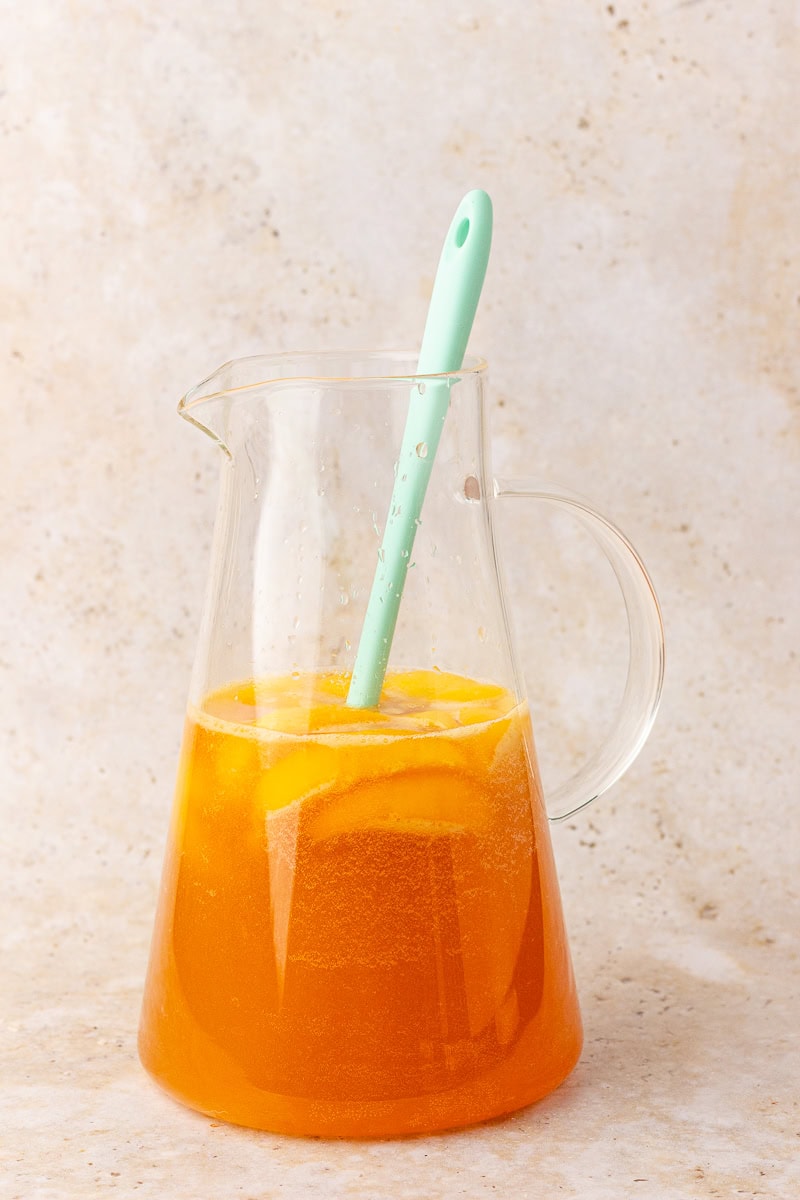 Glass pitcher of Georgia peach sangria with frozen peach slices and a teal spoon, ready to serve.