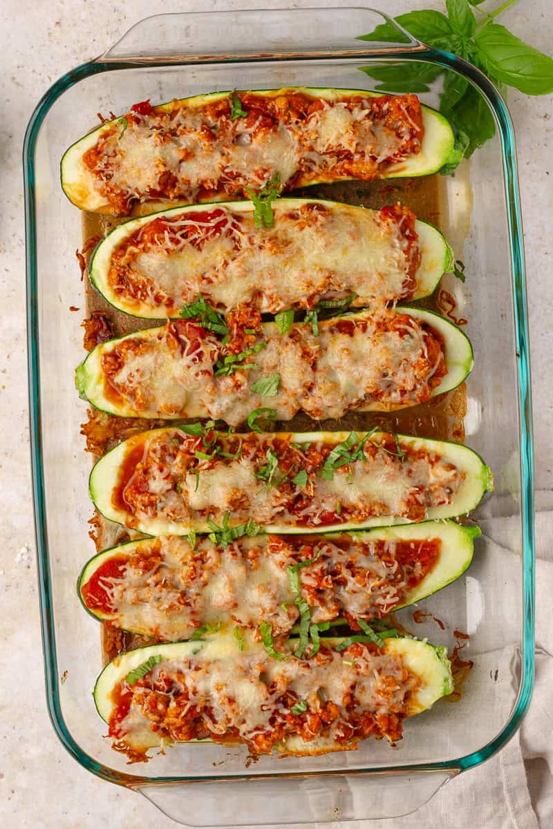 Baked zucchini boats topped with melted mozzarella and fresh basil in a glass dish.