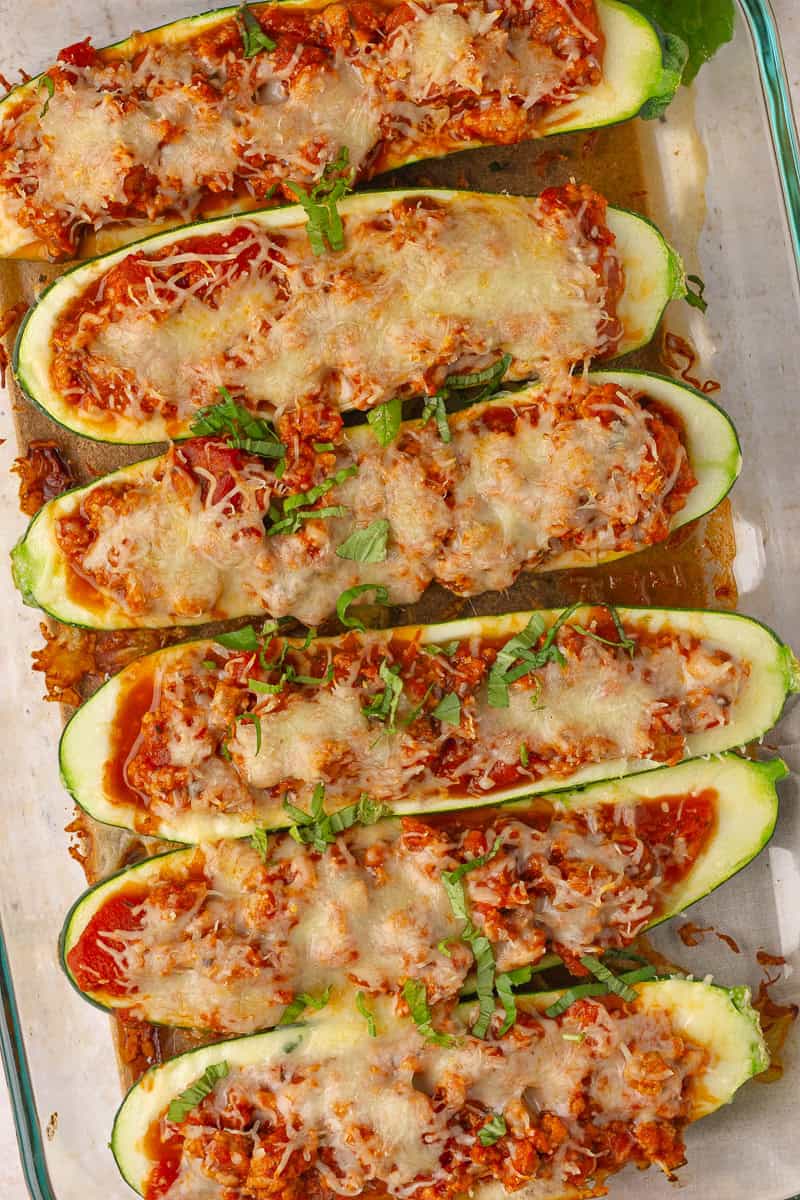 Close-up of baked zucchini boats with cheesy bolognese filling and chopped basil on top.