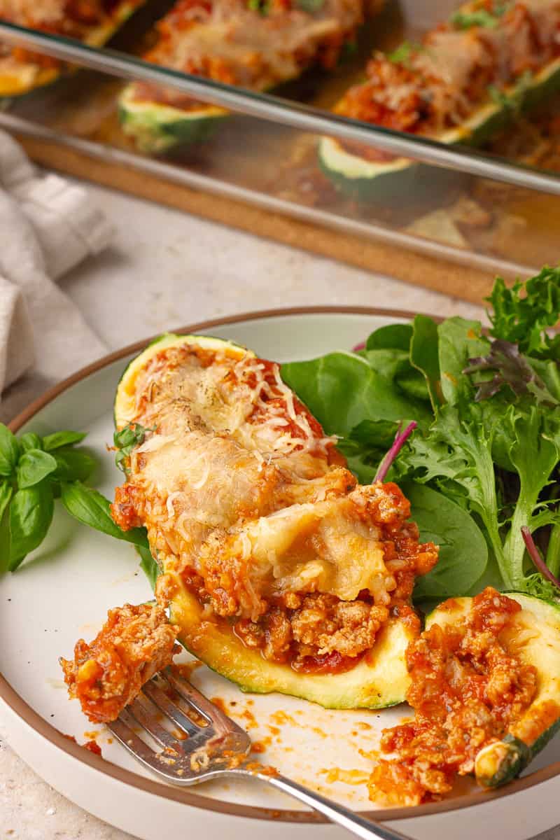 A plated zucchini boat served with mixed greens, with a fork taking a bite.