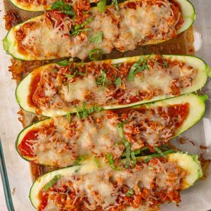 Overhead view of six cheesy zucchini boats lined up in a glass baking dish, garnished with basil.