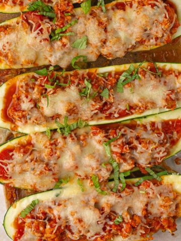 Overhead view of six cheesy zucchini boats lined up in a glass baking dish, garnished with basil.