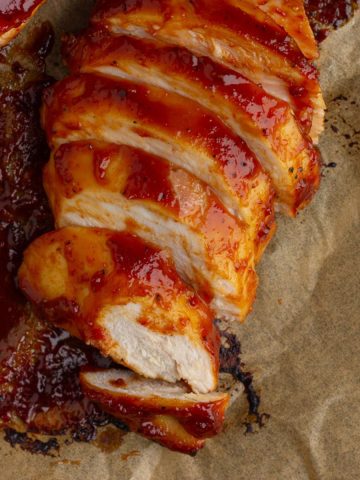 Close-up of juicy, sliced BBQ chicken breast with sticky sauce and golden edges.