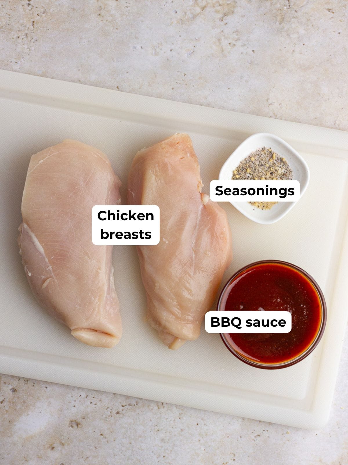 Labeled ingredients for air fryer BBQ chicken including raw chicken breasts, BBQ sauce, and dry seasoning on a cutting board.