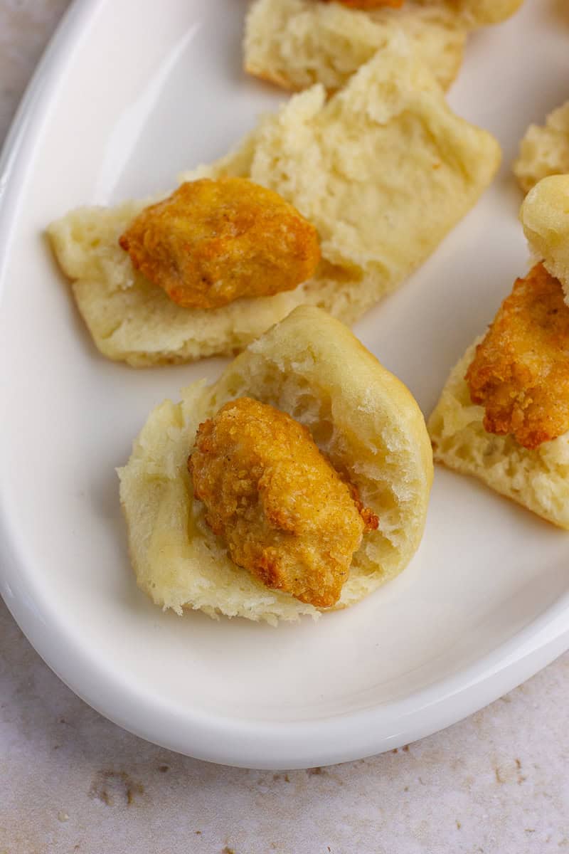 Fluffy dinner rolls sliced open with crispy nuggets placed inside for assembling.