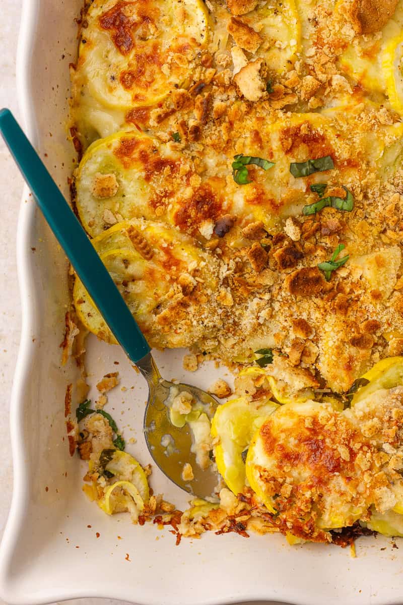 A close-up of cheesy baked yellow squash casserole with a golden crumb topping and a spoon ready to serve.
