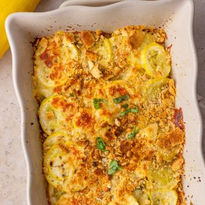 Golden-baked squash casserole topped with herbs and crispy crumbs, served in a white ceramic baking dish.