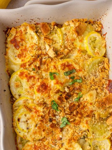 Golden-baked squash casserole topped with herbs and crispy crumbs, served in a white ceramic baking dish.