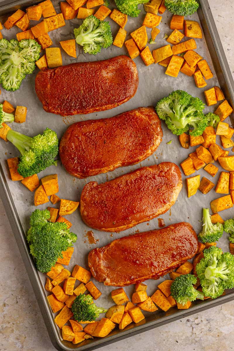 Pork chops, sweet potatoes, and broccoli arranged on a sheet pan before baking.
