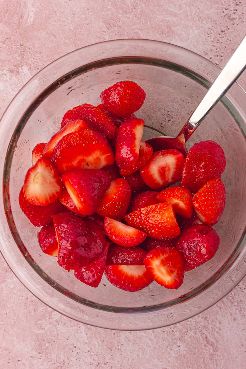 Fresh strawberries are halved and tossed in a bowl, ready to be roasted.