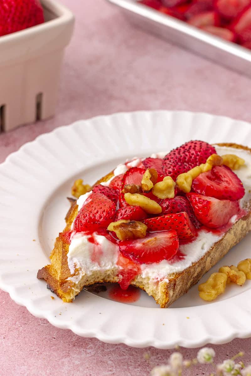 Roasted strawberries are served on toast with ricotta and walnuts on a white plate.