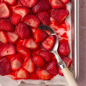 Close-up of roasted strawberries in their syrup with a serving spoon on the pan.