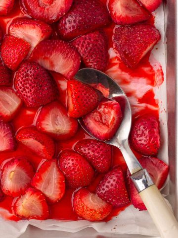 Close-up of roasted strawberries in their syrup with a serving spoon on the pan.