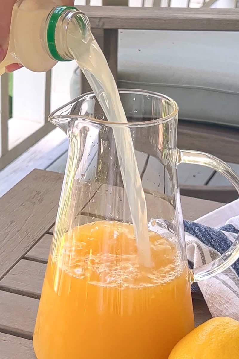Lemonade being poured into a pitcher of peach juice to create southern peach lemonade.

