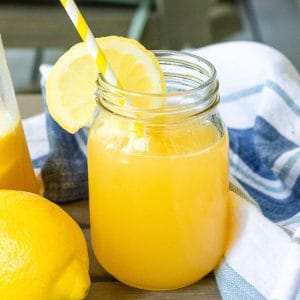 A styled shot of peach lemonade in a mason jar with a lemon slice and straw, perfect for summer.