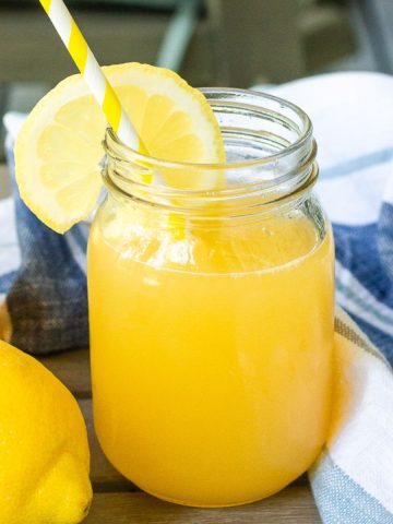 A styled shot of peach lemonade in a mason jar with a lemon slice and straw, perfect for summer.