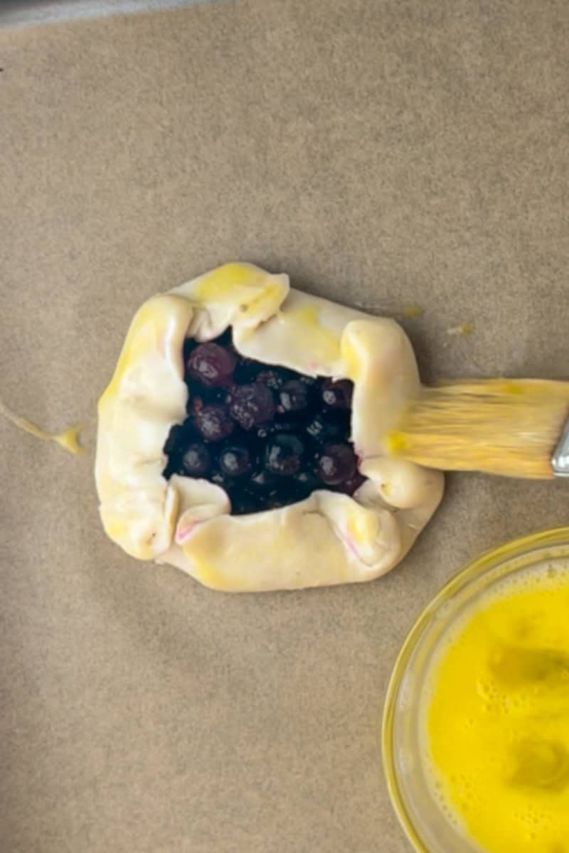 A folded blueberry lemon galette gets a brush of egg wash before heading into the oven.