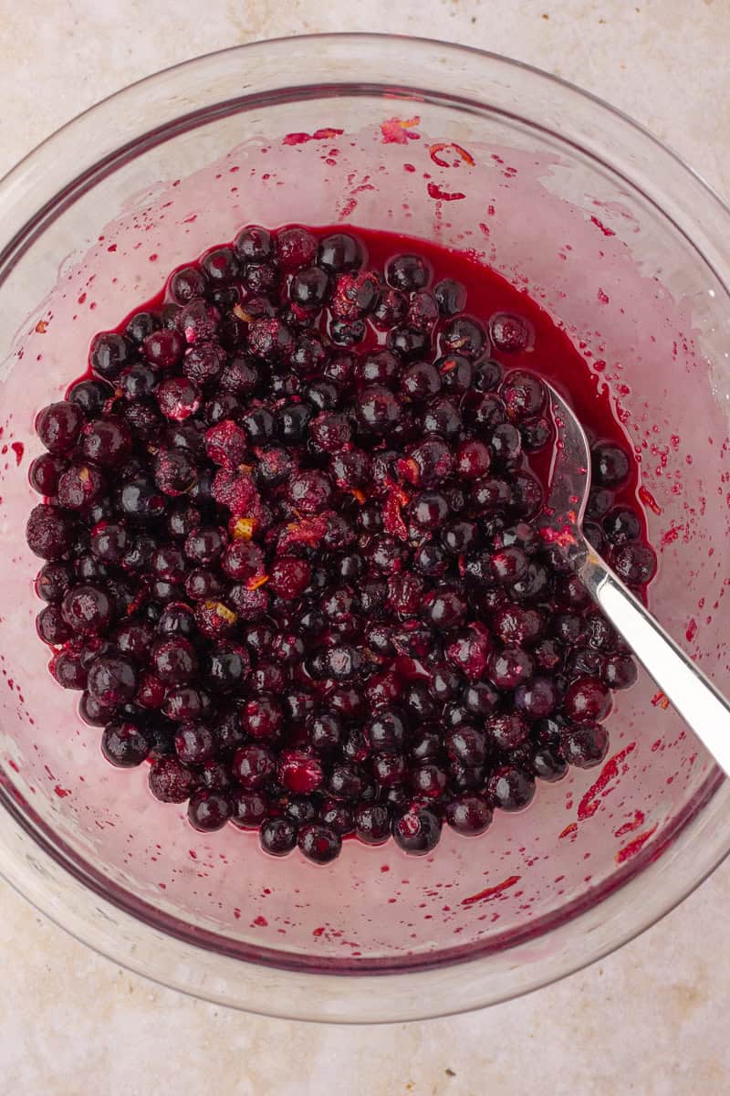 A glass bowl of frozen wild blueberries is tossed with sugar and lemon zest.